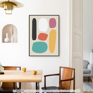 May include: Abstract art print featuring a black framed artwork with colorful, rounded shapes. The shapes include black, white, red, pink, yellow, and teal on a beige background. The artwork hangs on a white wall in a dining room setting.