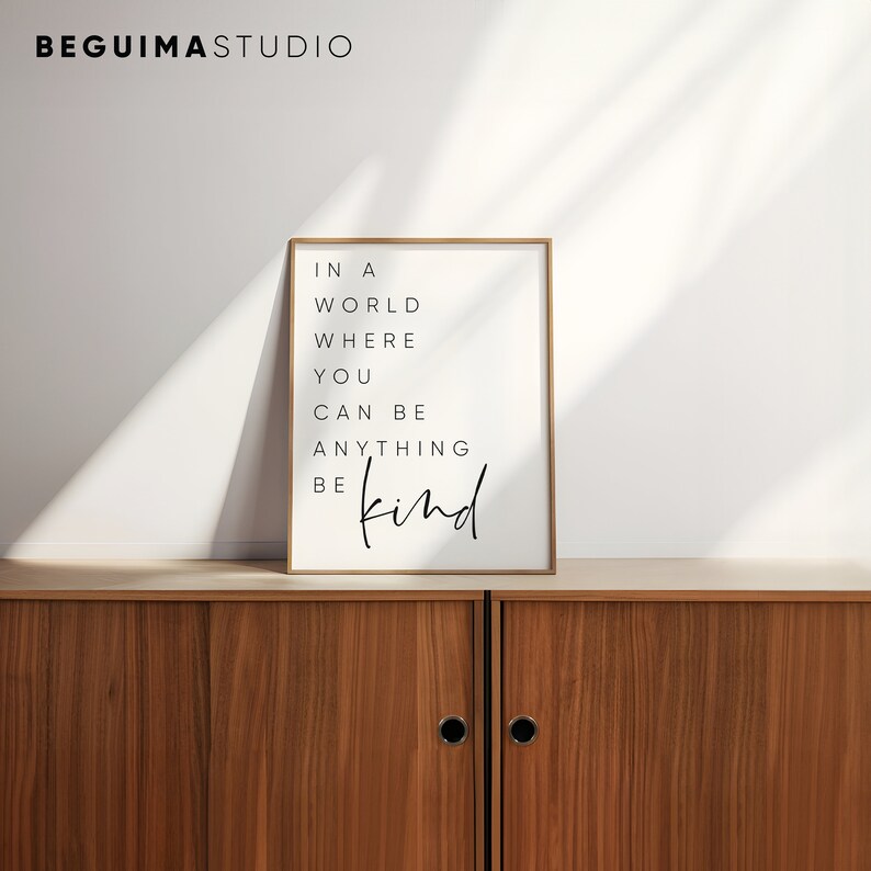 May include: A framed print with the text "In a world where you can be anything be kind" in black lettering on a white background.