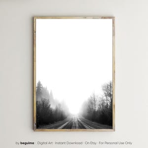 May include: Black and white framed print of a misty road leading into the distance. The road is flanked by trees and shrouded in fog, creating a sense of depth and mystery. The print is in a wooden frame.