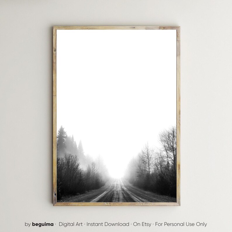 May include: Black and white framed print of a misty road leading into the distance. The road is flanked by trees and shrouded in fog, creating a sense of depth and mystery. The print is in a wooden frame.