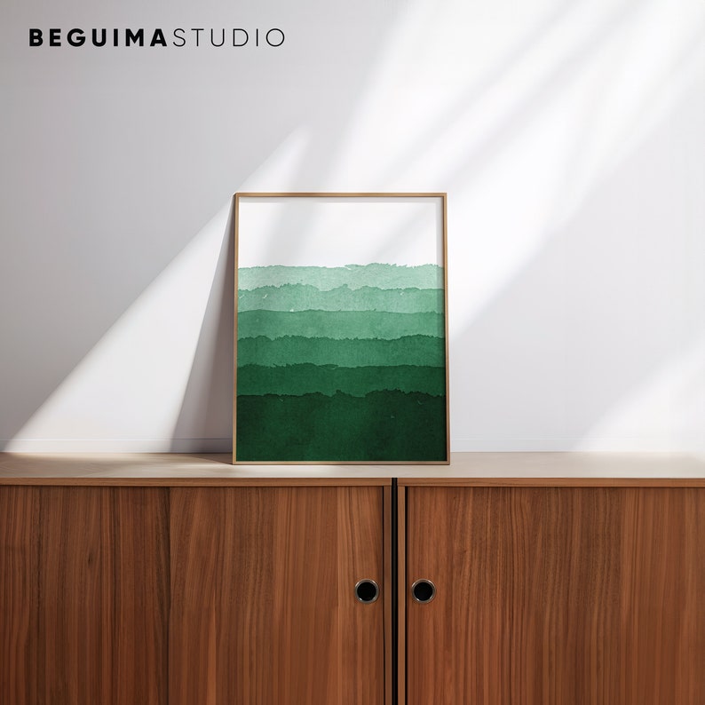 May include: A framed art print featuring a watercolor design of layered green hues. The artwork has a gold frame and is displayed on a wooden cabinet. The top of the print has a white background, with the text "BEGUIMA STUDIO" at the top.