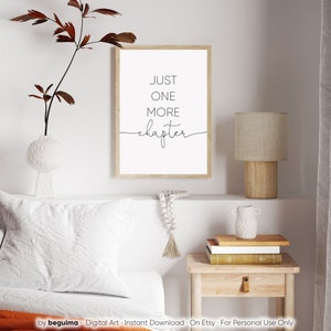 Peut inclure: Une impression encadr&eacute;e blanche avec du texte noir qui dit "JUST ONE MORE chapter" sur un mur blanc au-dessus d'un lit avec une t&ecirc;te de lit blanche et un oreiller blanc. Une table de chevet en bois avec une lampe et un vase est &agrave; droite du lit.