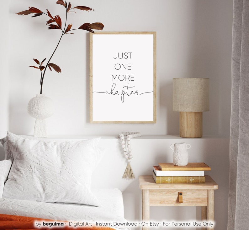 Peut inclure: Une impression encadr&eacute;e blanche avec du texte noir qui dit "JUST ONE MORE chapter" sur un mur blanc au-dessus d'un lit avec une t&ecirc;te de lit blanche et un oreiller blanc. Une table de chevet en bois avec une lampe et un vase est &agrave; droite du lit.