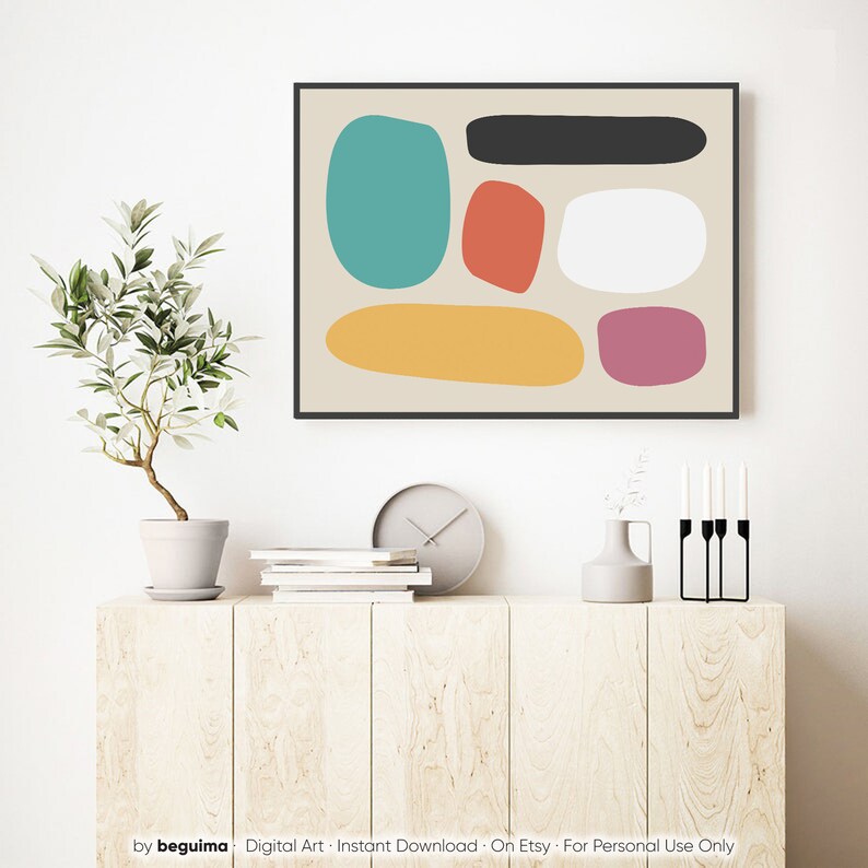 May include: Abstract art print featuring colorful, rounded shapes in teal, red, white, black, yellow, and purple on a beige background. The artwork is framed in a black border and displayed above a wooden cabinet with a plant, clock, and decorative items.