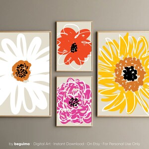 May include: Four framed floral art prints. The prints feature abstract flower designs in white, orange, pink, and yellow on a neutral background. The flowers have black and brown centers. The frames are a light wood color. The bottom of the image has the text "by beguima".