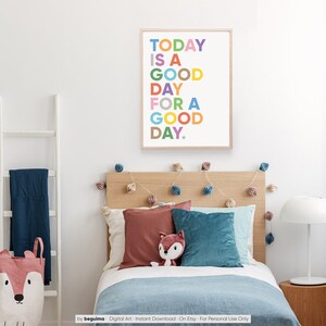 May include: A colorful printable wall art print with the text "TODAY IS A GOOD DAY FOR A GOOD DAY." The print is framed in a light wood frame and is hanging on a white wall above a bed with a wooden headboard.