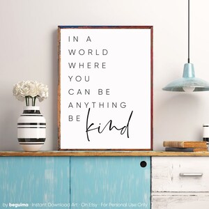 May include: A white framed print with black text that reads "In a world where you can be anything be kind".
