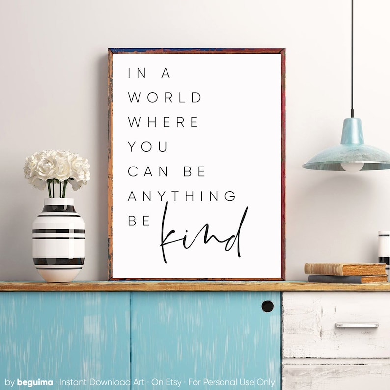 May include: A white framed print with black text that reads "In a world where you can be anything be kind".