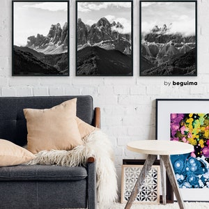 May include: Three framed black and white mountain landscape prints hang on a white brick wall. The artwork depicts rugged peaks with snow and clouds. The prints are above a gray sofa with beige pillows and a white fur throw.