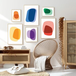 May include: Set of six abstract art prints featuring overlapping shapes in various colors, including yellow, orange, red, blue, green, and purple. The prints are displayed on a white wall in a living room setting.