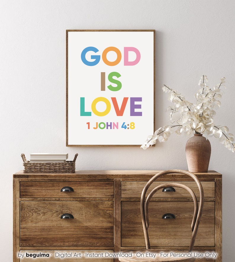 May include: A framed art print with the words "GOD IS LOVE" in colorful letters. Below the words is the text "1 JOHN 4:8". The print is displayed on a wooden dresser with a vase of white flowers.