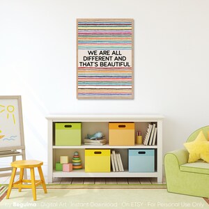 May include: A framed print featuring a design of horizontal, multi-coloured stripes and the words "WE ARE ALL DIFFERENT AND THAT'S BEAUTIFUL." The print hangs above a white bookcase with colourful storage boxes, a yellow stool, and a green armchair.
