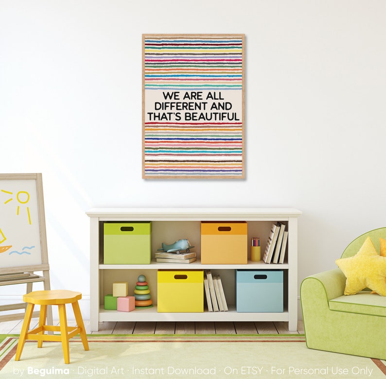 May include: A framed print featuring a design of horizontal, multi-coloured stripes and the words "WE ARE ALL DIFFERENT AND THAT'S BEAUTIFUL." The print hangs above a white bookcase with colourful storage boxes, a yellow stool, and a green armchair.
