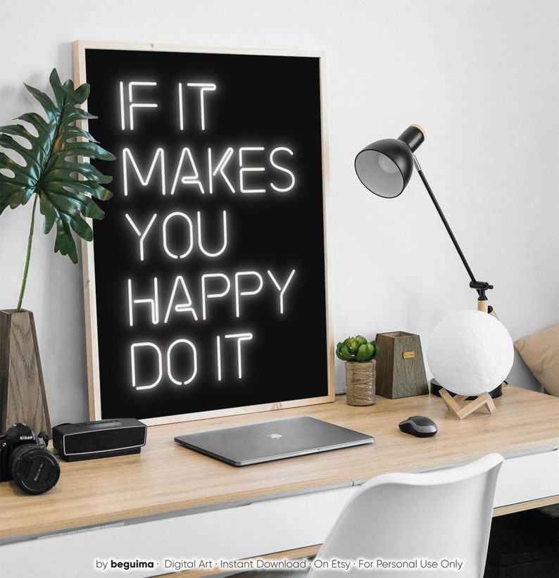 May include: A black framed print with the words "IF IT MAKES YOU HAPPY DO IT" in white neon-style lettering. The print is on a wooden desk with a laptop, lamp, and other decorative items.