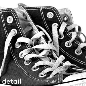 Puede incluir: Primer plano de zapatillas altas negras con cordones y costuras blancas. Las zapatillas tienen ojales met&aacute;licos y una parte superior de lona. La palabra "detail" est&aacute; impresa en blanco en la esquina inferior izquierda.
