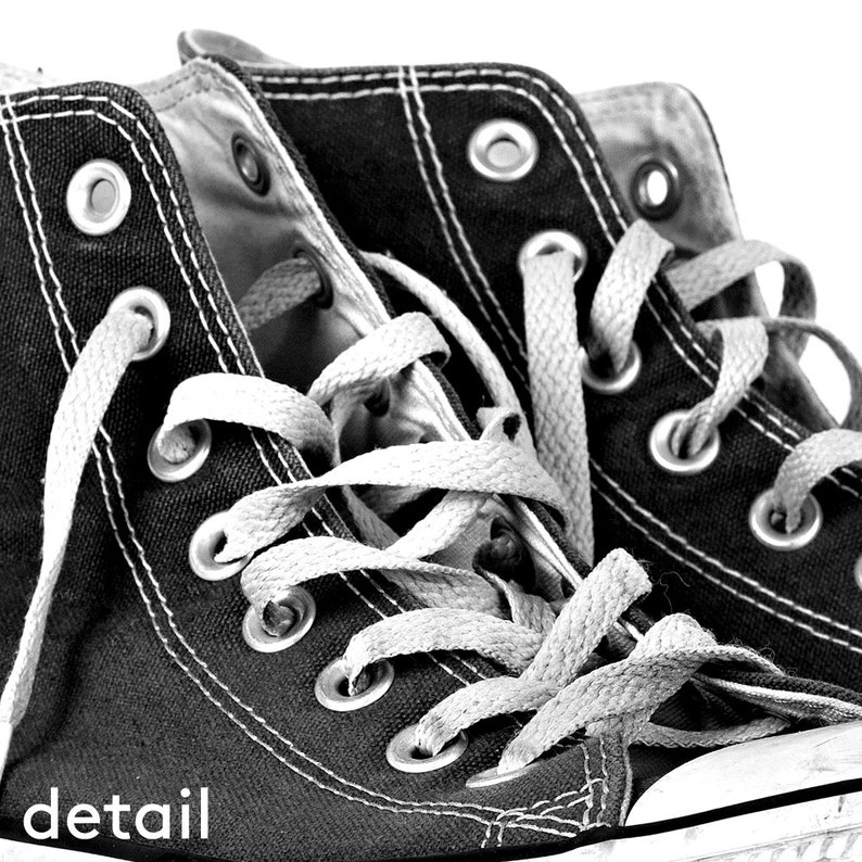 Puede incluir: Primer plano de zapatillas altas negras con cordones y costuras blancas. Las zapatillas tienen ojales met&aacute;licos y una parte superior de lona. La palabra "detail" est&aacute; impresa en blanco en la esquina inferior izquierda.