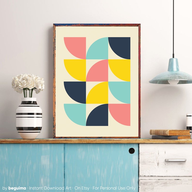 Puede incluir: Impresi&oacute;n art&iacute;stica geom&eacute;trica enmarcada con un patr&oacute;n de semic&iacute;rculos coloridos en rosa, amarillo, azul marino y turquesa sobre un fondo crema. La obra de arte se exhibe sobre un mueble azul. Tambi&eacute;n se ven un jarr&oacute;n con flores blancas y una l&aacute;mpara colgante azul claro.