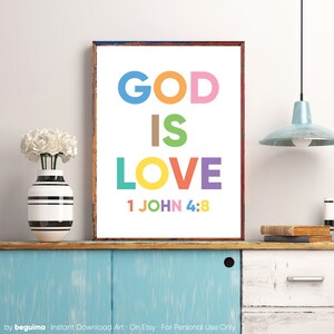 May include: A framed print with the words "GOD IS LOVE" in large, colorful letters. Below the text is "1 JOHN 4:8". The print is displayed on a blue cabinet with a vase of white flowers and a black and white striped vase.