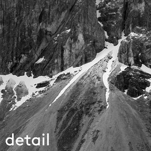 May include: Black and white photograph of a mountain range with snow patches. The image is a close-up, showing the texture of the rocks and the contrast between the dark mountains and the white snow. The word "detail" is at the bottom.