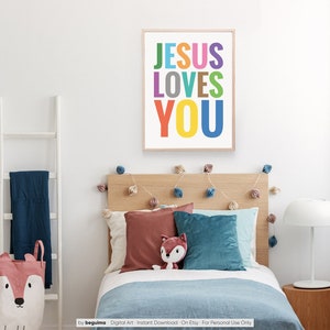 Może przedstawiać: Kolorowy, drukowany obraz na ścianę z tekstem "JESUS LOVES YOU" w tęczy kolor&oacute;w. Obraz jest wyświetlany w sypialni z ł&oacute;żkiem, poduszkami i lampą.