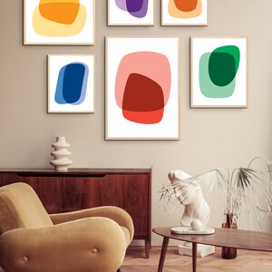 May include: Set of six abstract art prints featuring overlapping geometric shapes in various colors, including red, orange, yellow, green, blue, and purple. The prints are framed and displayed on a wall in a modern living room setting.