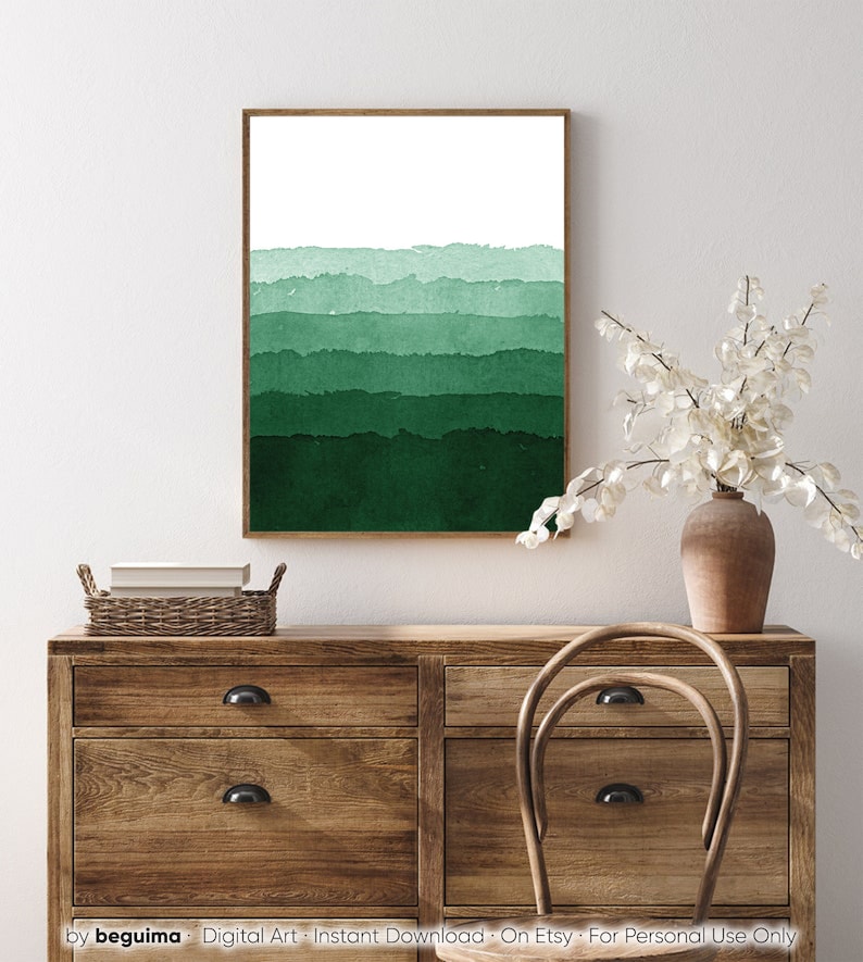 May include: A framed watercolor print featuring horizontal bands of varying shades of green, transitioning from light to dark. The artwork is displayed on a white wall above a wooden dresser. The print has a brown frame.