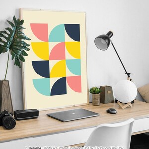 Puede incluir: Un cuadro enmarcado con un dise&ntilde;o geom&eacute;trico de semic&iacute;rculos en rosa, azul, amarillo y azul marino sobre un fondo crema. La obra de arte se exhibe en un escritorio de madera, junto con una l&aacute;mpara de escritorio negra, un ordenador port&aacute;til y otros accesorios de oficina.