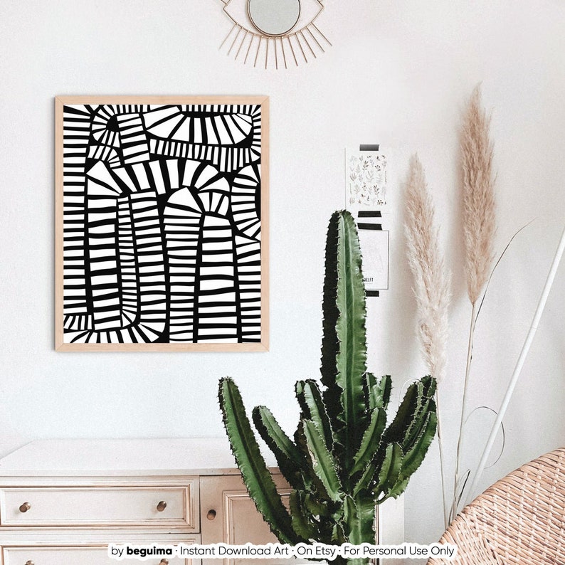 May include: A framed black and white abstract art print with geometric shapes. The artwork features a series of vertical and arched lines, creating a bold contrast. The print is displayed on a white wall, complemented by a cactus and decorative elements.
