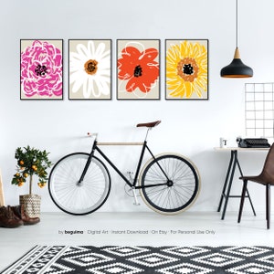May include: Four framed floral art prints in pink, white, orange, and yellow. The artwork features abstract flower designs on a neutral background. A black bicycle with white tires is leaning against the wall. The text "by beguima" is visible.