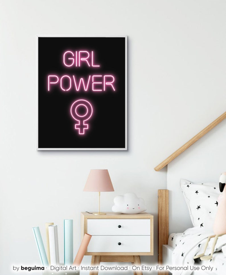 May include: A framed art print featuring the words "GIRL POWER" in pink neon-style lettering on a black background, with a pink Venus symbol below. The print is displayed on a white wall above a bedside table.
