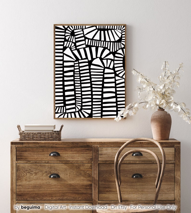 May include: Abstract black and white art print in a wooden frame. The artwork features a geometric design with vertical and curved lines. The print is displayed above a wooden dresser with a wicker basket and a vase of white flowers.