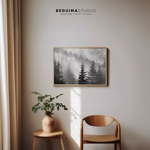 May include: A black and white watercolor painting of a foggy forest with tall pine trees. The painting is framed in a light wood frame and is hanging on a white wall.
