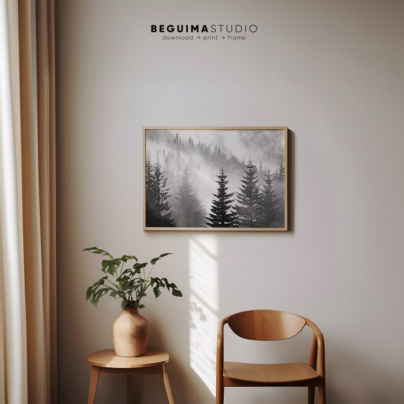 May include: A black and white watercolor painting of a foggy forest with tall pine trees. The painting is framed in a light wood frame and is hanging on a white wall.