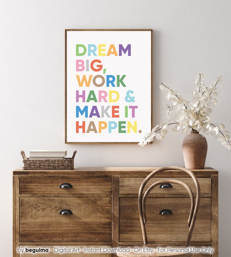 May include: A motivational quote in a colorful print reads "Dream Big, Work Hard & Make It Happen." The print is framed and hanging on a wall above a wooden dresser.