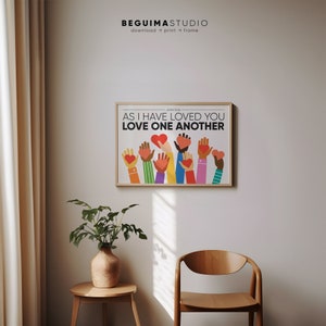 May include: A colorful print with the text "As I have loved you, love one another" and the Bible verse John 13:34. The print features a group of hands holding red hearts, each hand is a different skin tone.