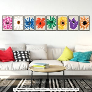 May include: A set of eight framed prints featuring colorful abstract flower illustrations. The prints are arranged in a row on a white wall above a white couch with pillows.