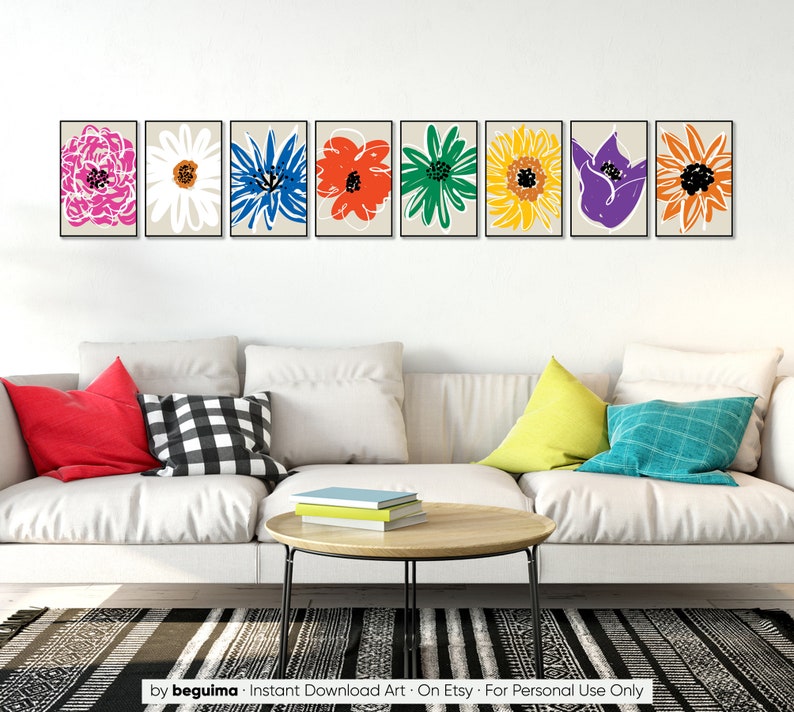 May include: A set of eight framed prints featuring colorful abstract flower illustrations. The prints are arranged in a row on a white wall above a white couch with pillows.