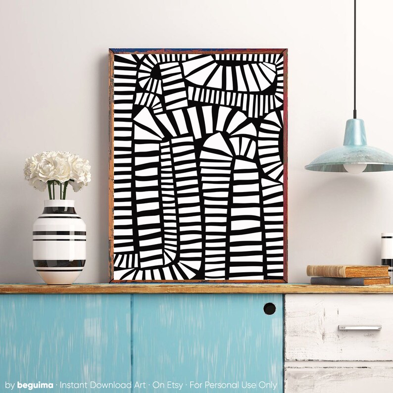 May include: Abstract black and white art print in a wooden frame. The artwork features a geometric design with curved and straight lines. A striped vase with white flowers sits on a blue cabinet. The text "by beguima" is at the bottom.