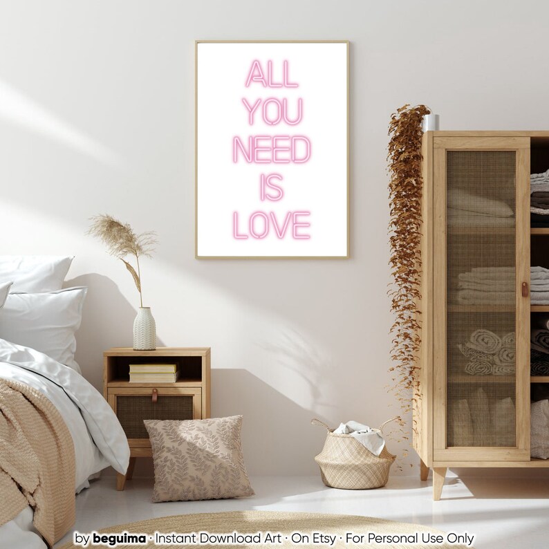 May include: A framed art print with the words "ALL YOU NEED IS LOVE" in pink neon-style lettering. The artwork is displayed in a bedroom setting, with a neutral color palette and natural wood furniture.