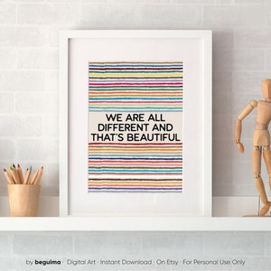 May include: Framed art print with the message "WE ARE ALL DIFFERENT AND THAT'S BEAUTIFUL". The artwork features horizontal stripes in various colours. A wooden artist's mannequin and pencils in a wooden cup are visible.