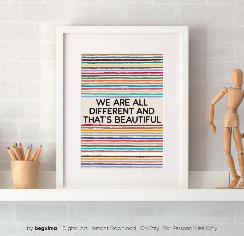 May include: Framed art print with the message "WE ARE ALL DIFFERENT AND THAT'S BEAUTIFUL". The artwork features horizontal stripes in various colours. A wooden artist's mannequin and pencils in a wooden cup are visible.