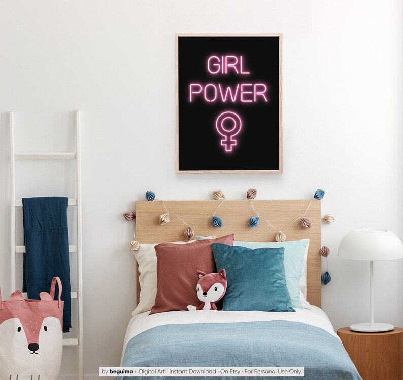 May include: A framed print with the words "GIRL POWER" in pink neon lettering, above a pink female symbol, against a black background. The print hangs above a bed with pillows and a stuffed fox. A white ladder and a fox-themed storage bag are visible.