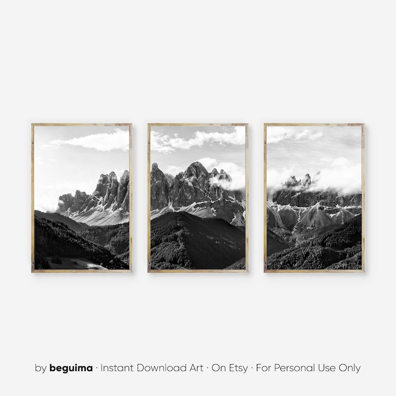 May include: A set of three framed black and white landscape prints. Each print features a mountain range with peaks, clouds, and a forested valley. The frames have a light wood finish. The prints are a minimalist style.