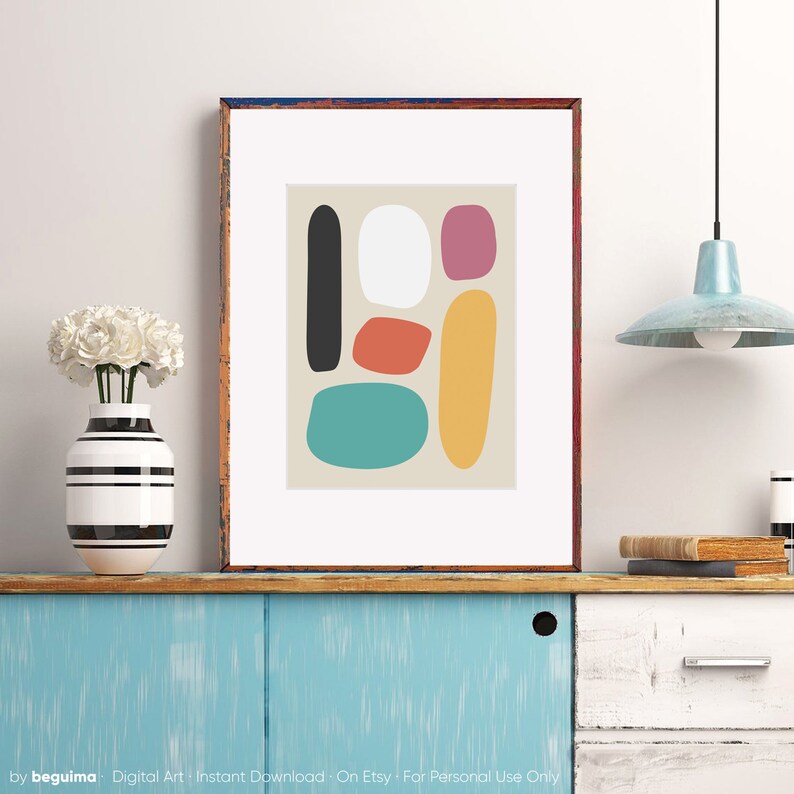 May include: Abstract art print featuring a beige background with colorful, rounded shapes in black, white, red-orange, teal, yellow, and magenta. The artwork is framed in a brown wooden frame and displayed on a blue cabinet.