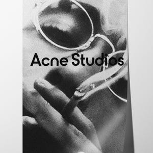 May include: Black and white image featuring the text "Acne Studios". The image shows a person wearing round sunglasses and holding a cigarette. The image is a close-up shot.