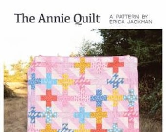 Puede incluir: Una colcha rosa y blanca con un patrón de signos más coloridos. La colcha está hecha con octavos de tela, cuartos de tela o recortes. La colcha está disponible en tamaños de bebé, regazo, doble, queen y king. La colcha se llama "The Annie Quilt" y es un patrón de Erica Jackman. El texto "Kitchen Table Quilting" está en la parte inferior de la imagen.