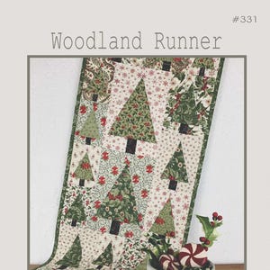 May include: A quilted table runner with a woodland theme, featuring green Christmas trees on a cream background with red floral accents. The runner measures 14 inches by 54.5 inches. A white mug with "MERRY" text and peppermint candies are in the foreground.
