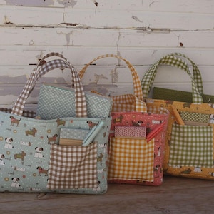 May include: Three handmade tote bags with coordinating pouches. The bags feature a variety of patterns, including dog prints, gingham, and solid colors. Each bag has a front pocket and matching handles. The bags are displayed against a white wooden background.