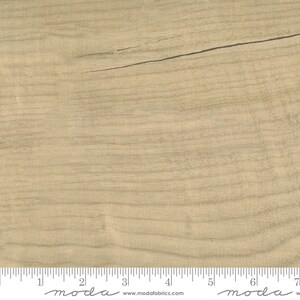 May include: A close-up of a light brown woodgrain fabric with a subtle sheen. The fabric is measured in inches with the text "moda" printed on the ruler.