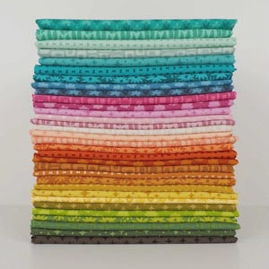 May include: A tall stack of folded fabric squares arranged in a spectrum of colors. The collection includes shades of teal, blue, pink, peach, orange, yellow, and green, each featuring repeating geometric, floral, and star-shaped patterns.